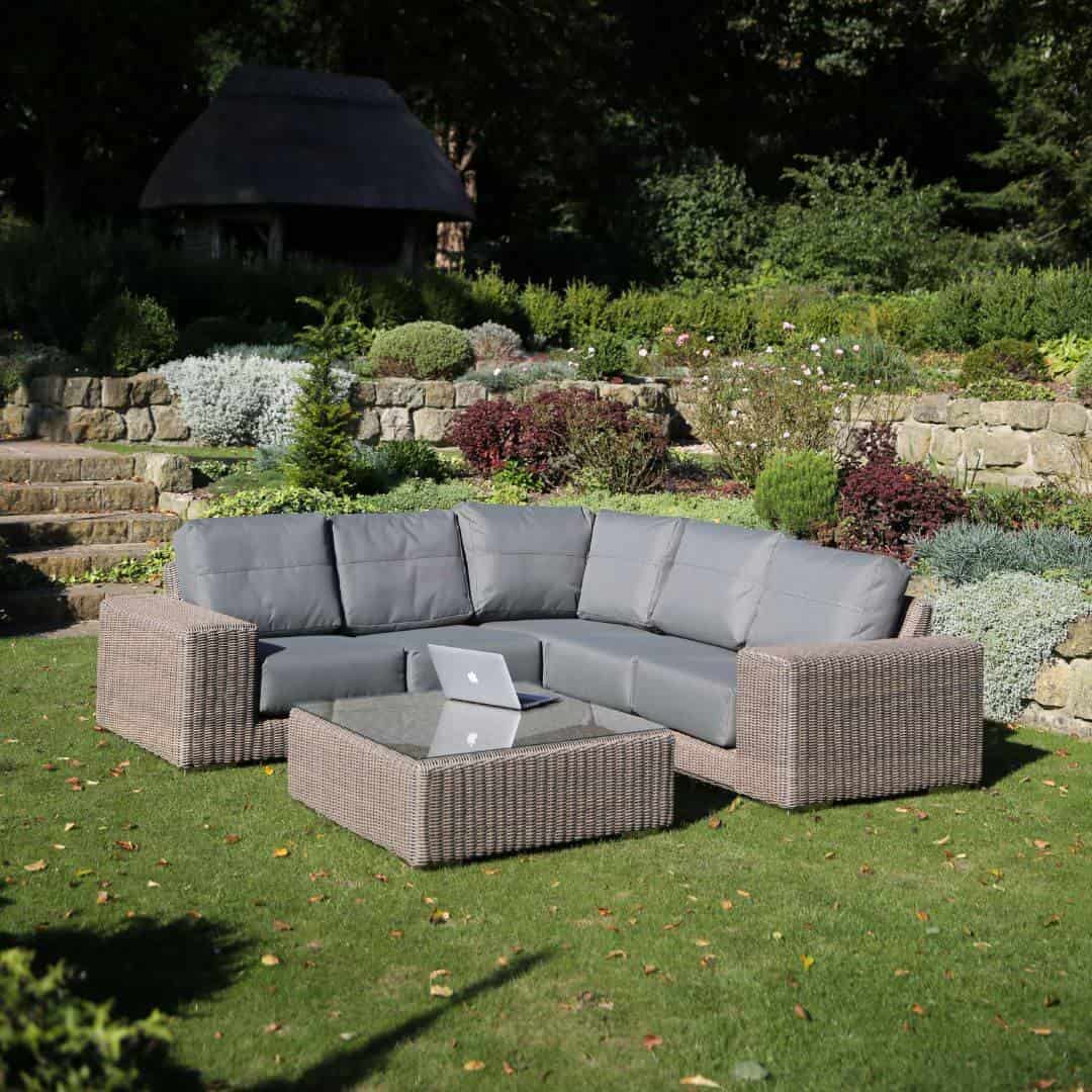 Beige rattan corner sofa with matching coffee table and grey cushions.