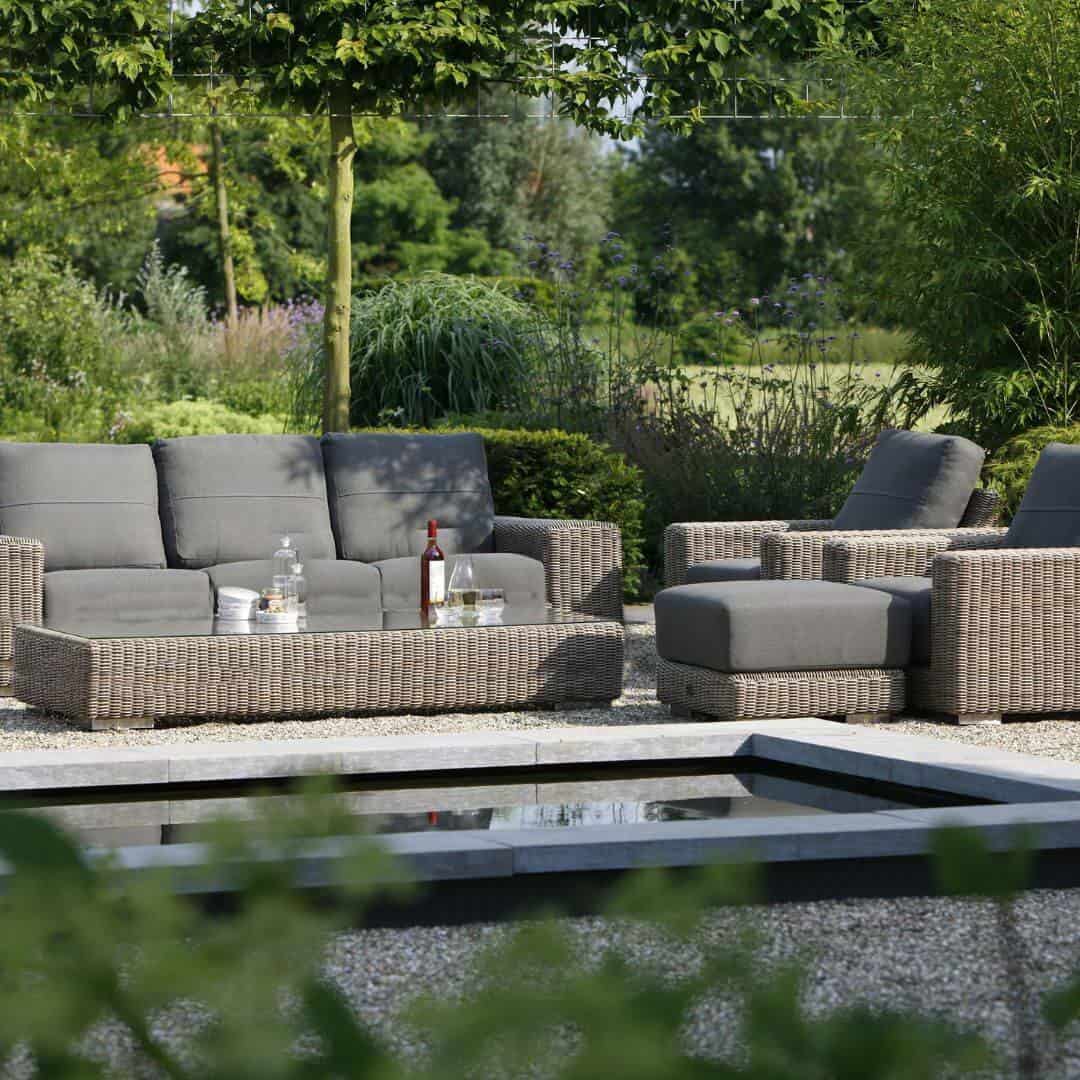 Beige rattan wicker lounge set with three seater bench, two armchair, footstool and coffee table.