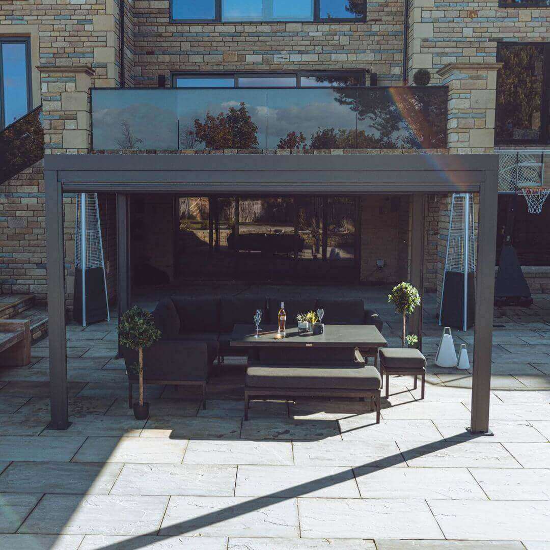 Front view of a grey aluminium pergola with louvred roof. An outdoor fabric corner dining set sits under the pergola.