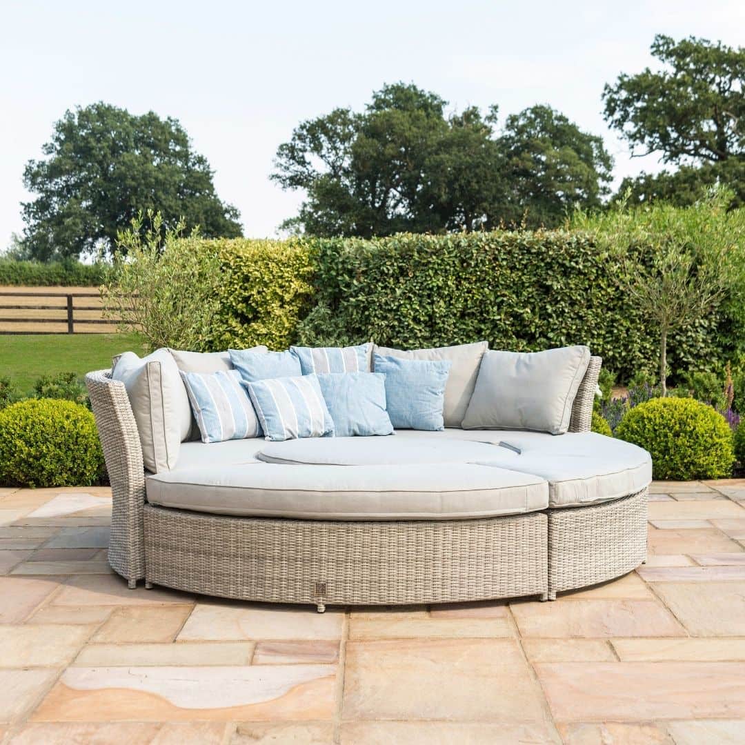 Light grey rattan lifestyle suite with a curved sofa, curved bench and a rising table - pushed together as a day bed