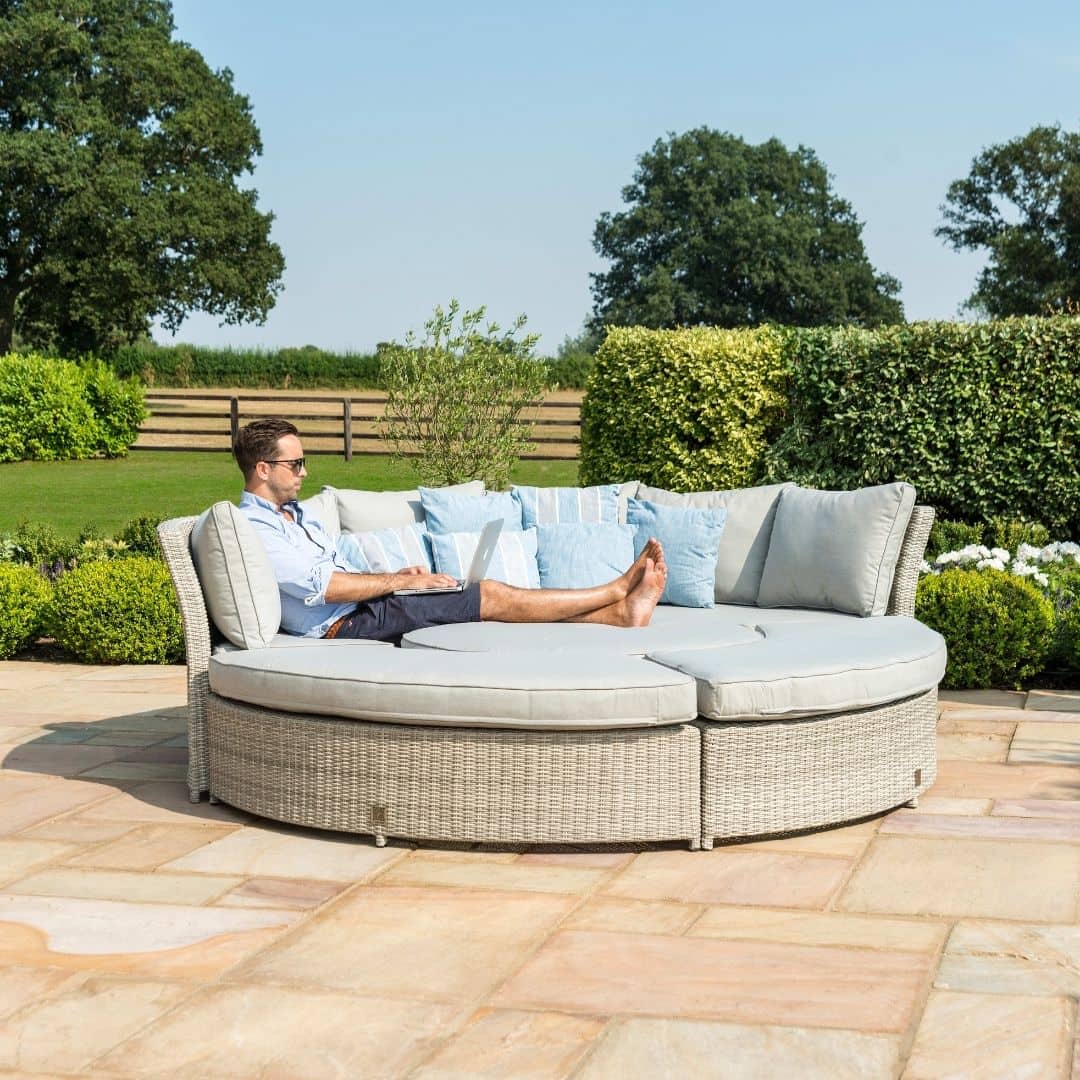 Light grey rattan lifestyle suite with a curved sofa, curved bench and a rising table - pushed together as a day bed