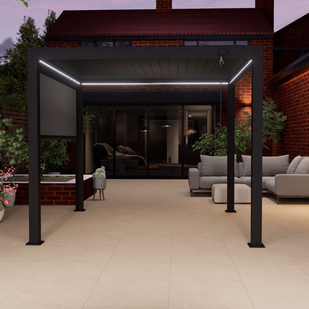 Front view of a grey aluminium pergola with louvred roof. The white LED lights underneath the roof panel are turned on.