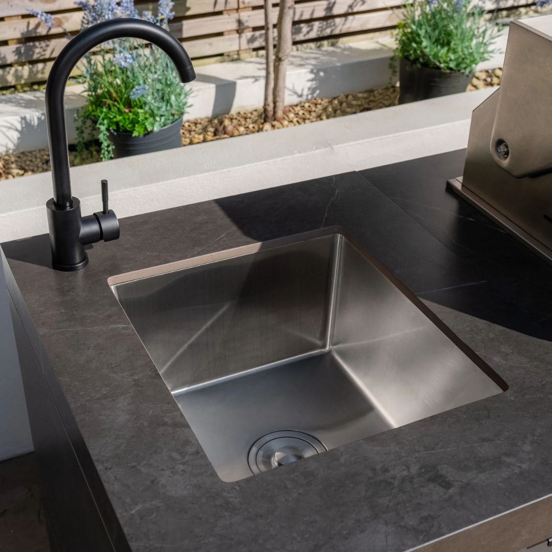 Grey outdoor kitchen unit with a bbq top unit, sink and fridge.
