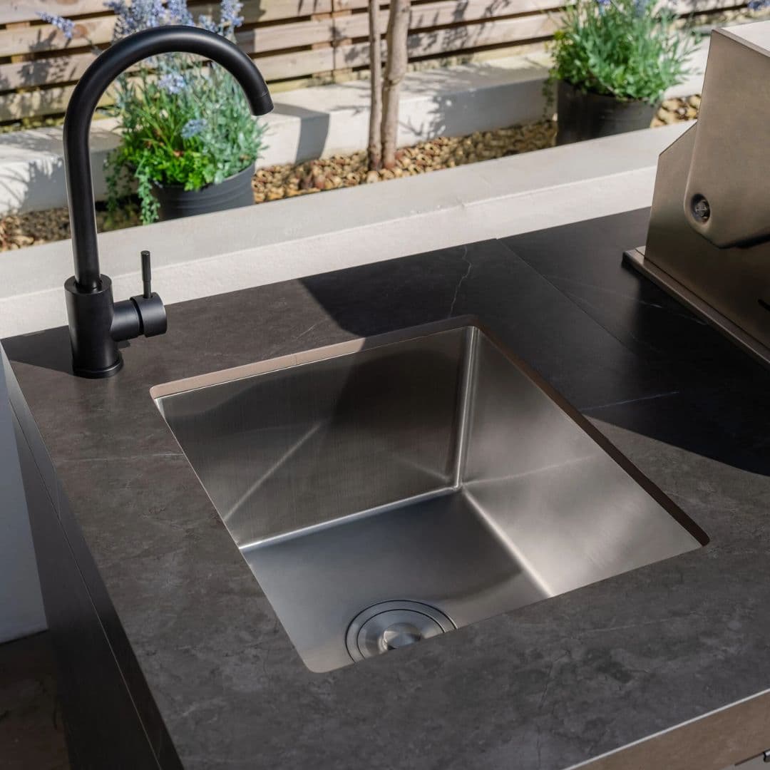 Grey outdoor kitchen unit with a bbq top unit, sink and fridge.