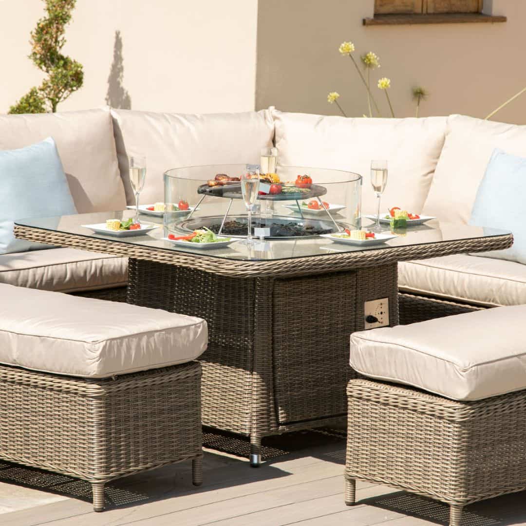 Close up of a natural coloured rattan corner sofa with two matching benches and square fire pit table.