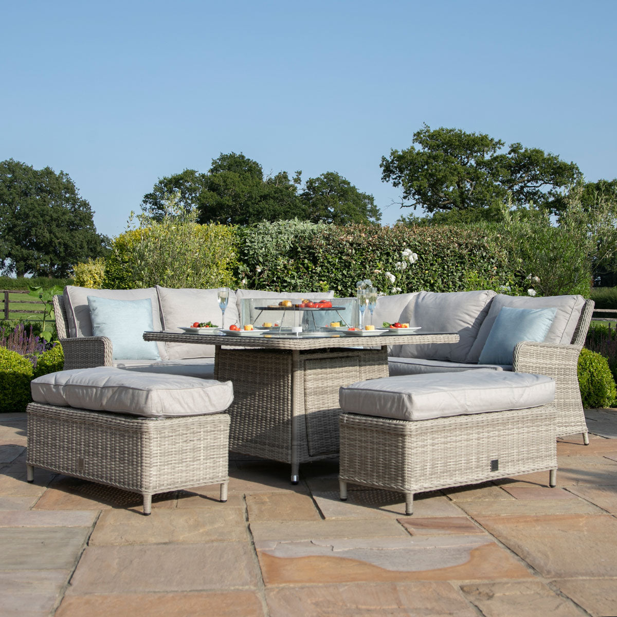 Light grey coloured rattan corner sofa with two matching benches and square fire pit table.