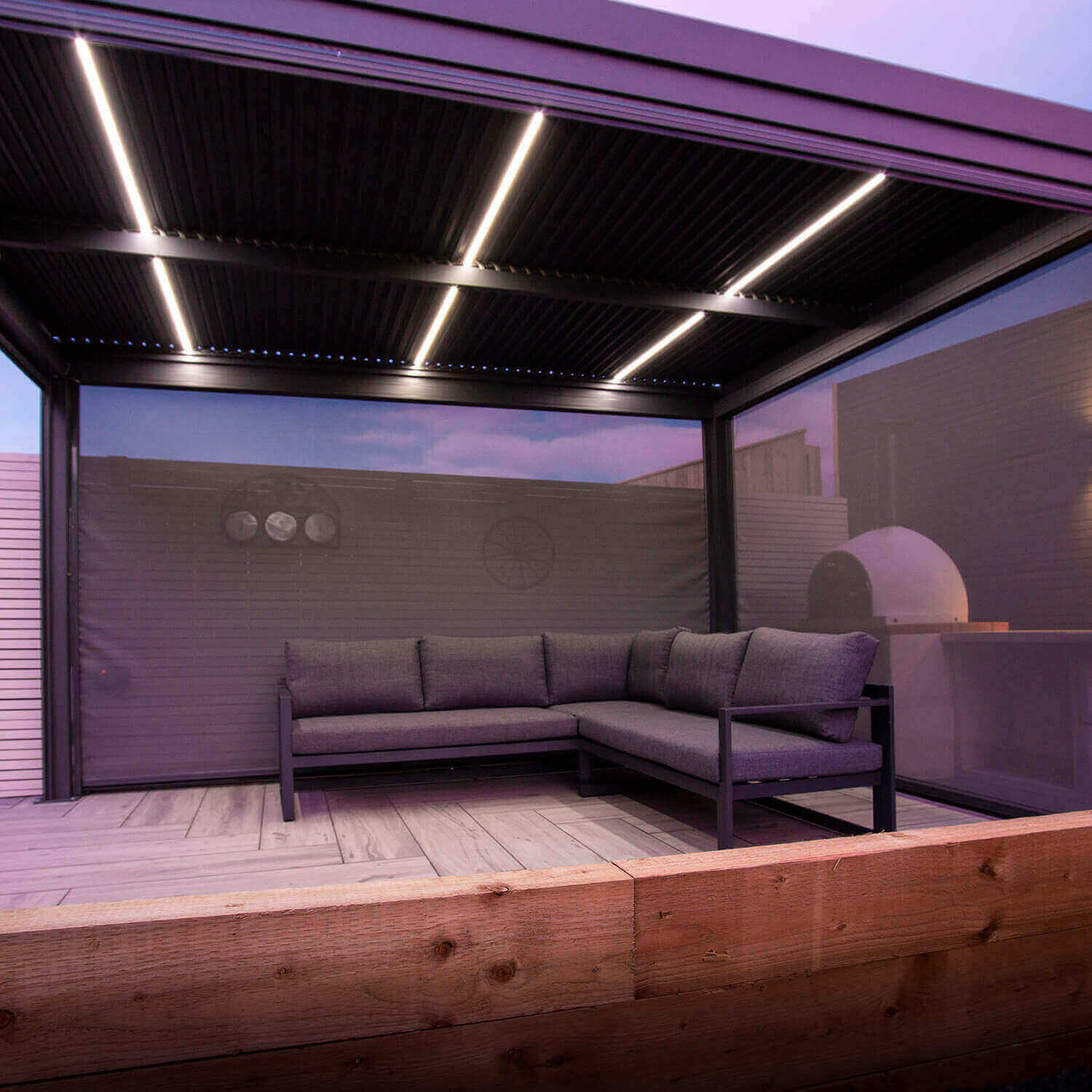 Side view of the motorised louvred roof with white LED lights turned on. Two additional privacy screens attached to the grey aluminium pergola.