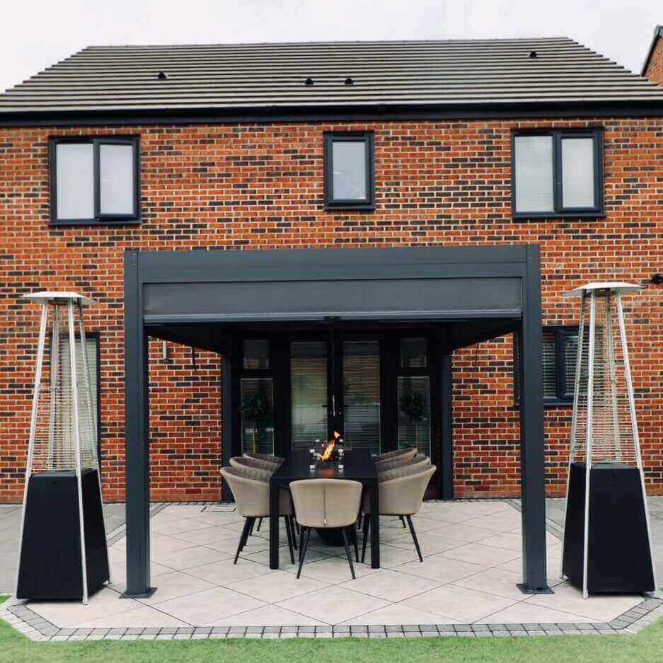 Front view of a 3m x 3m anthracite grey aluminium pergola with manual louvred roof. The pergola is against the side of a two storey house.
