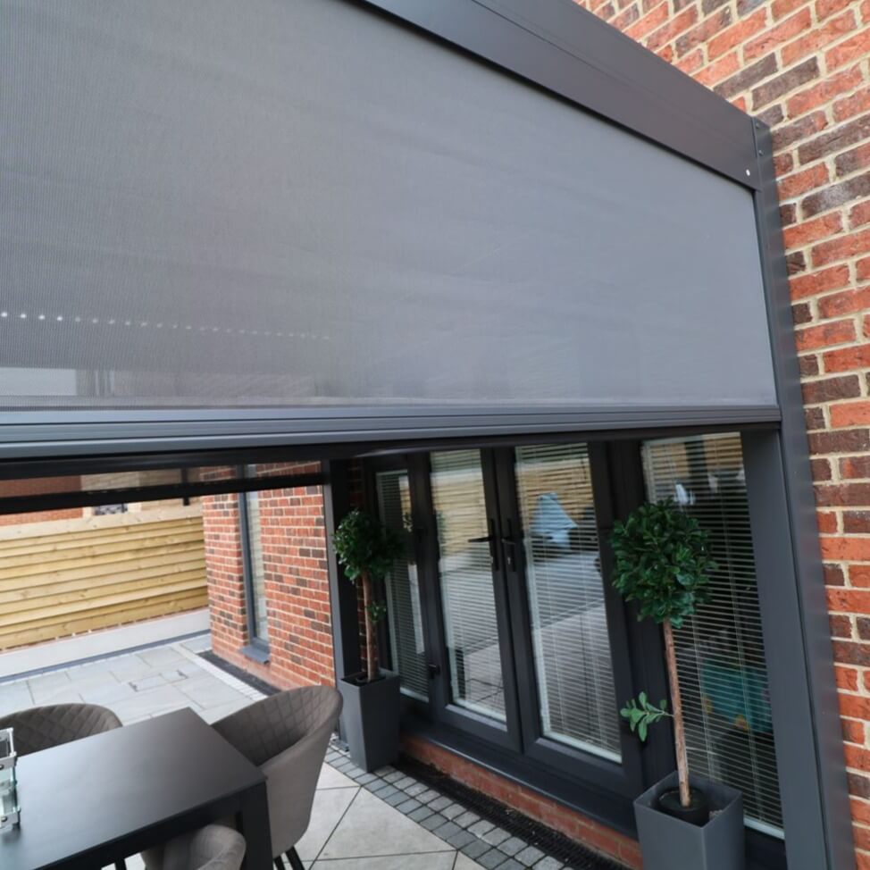 Close up of a Textilene privacy screen attached to a grey aluminium pergola with louvred roof.
