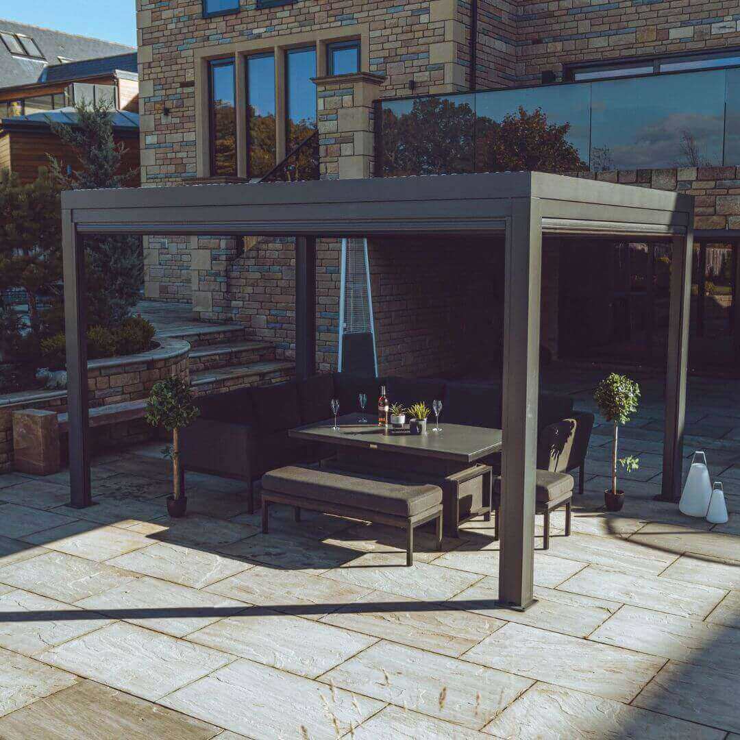 Side view of a grey aluminium pergola with louvred roof. An outdoor fabric corner dining set sits under the pergola.