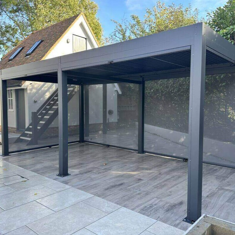 3m x 6m anthracite grey aluminium pergola with manual louvred roof, manual privacy screens and white LED lights. Three privacy screens pulled down.