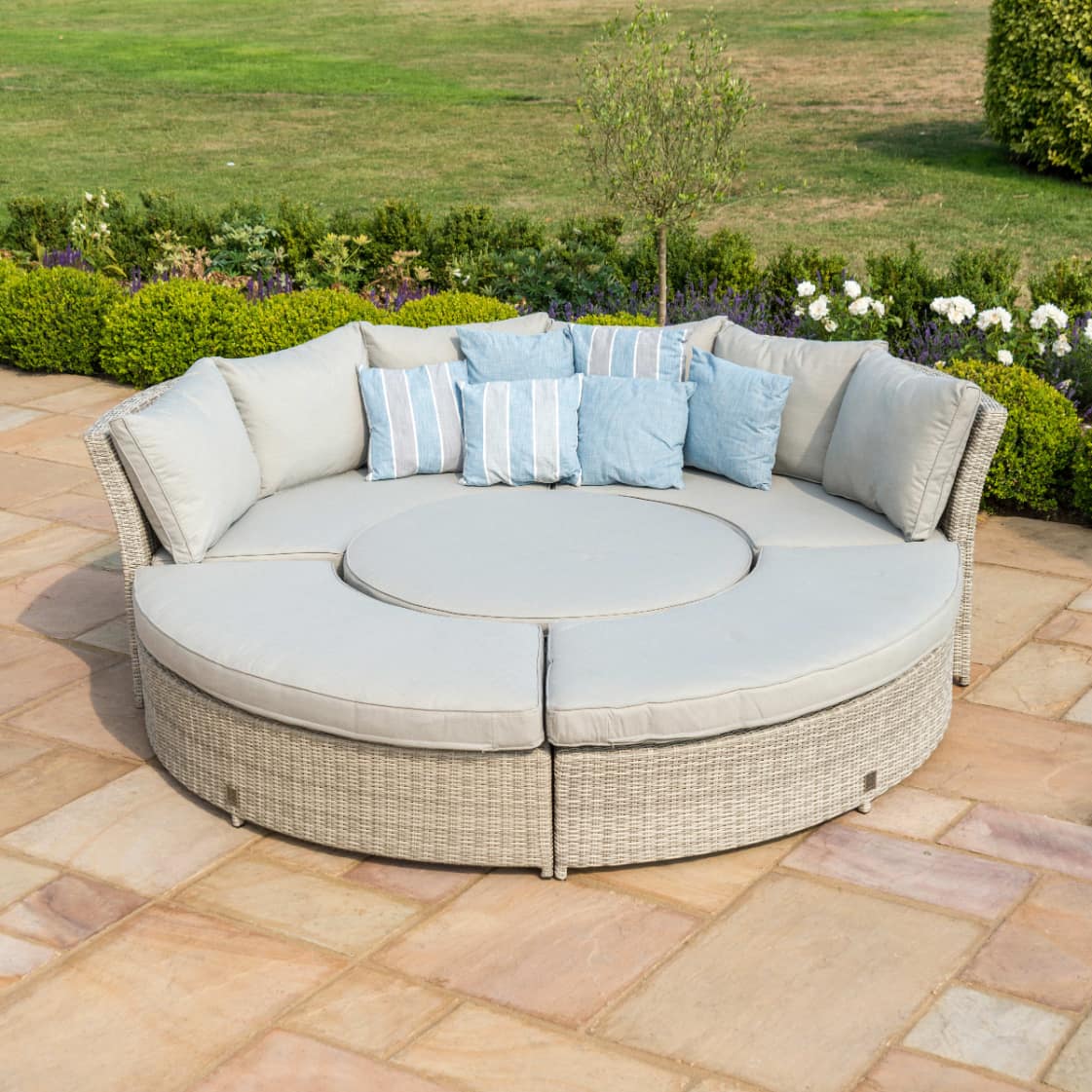 Light grey rattan lifestyle suite with a curved sofa, curved bench and a rising table - pushed together as a day bed