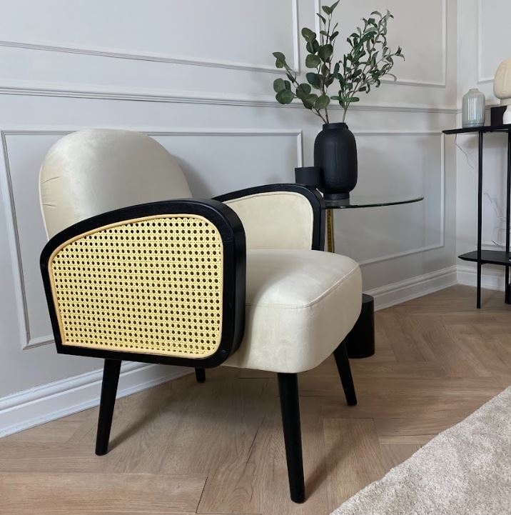 Natural velvet armchair with black wooden legs and rattan arms.