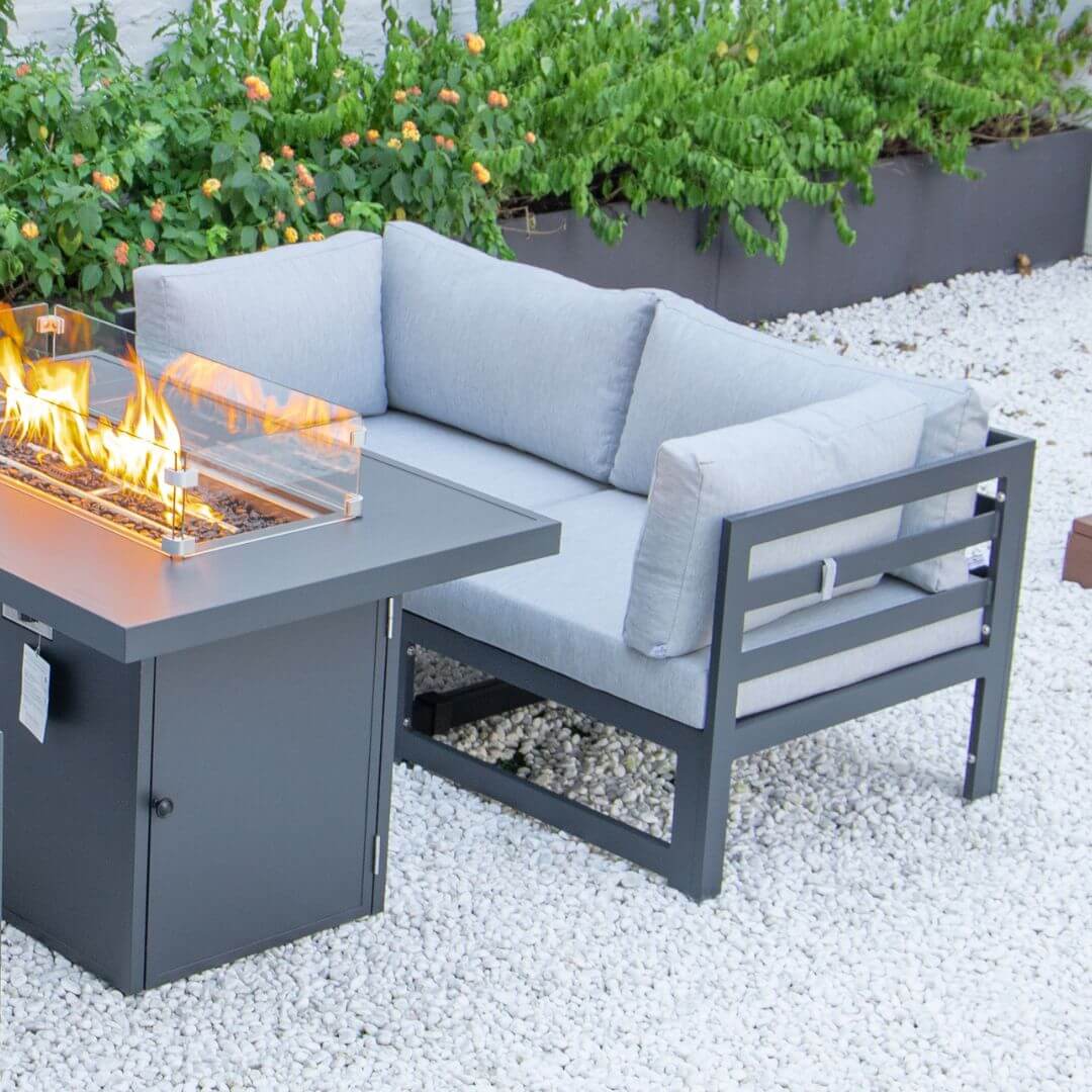 Close up of a grey aluminium 2 seat sofa with padded seat and back cushions. The corner of the fire pit table is in the frame.