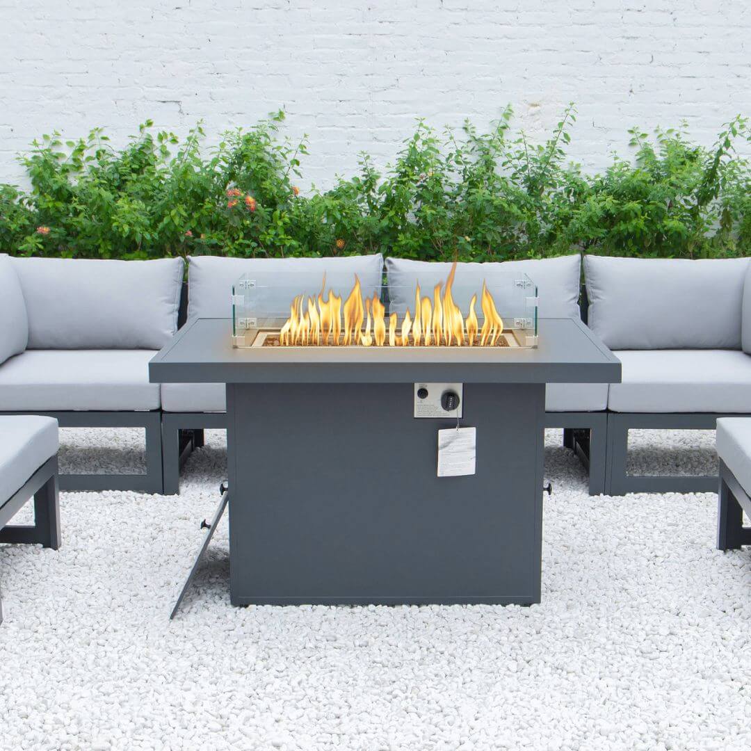 Close up of a grey aluminium fire pit table and 4 seat sofa with padded seat and back cushions in the background.