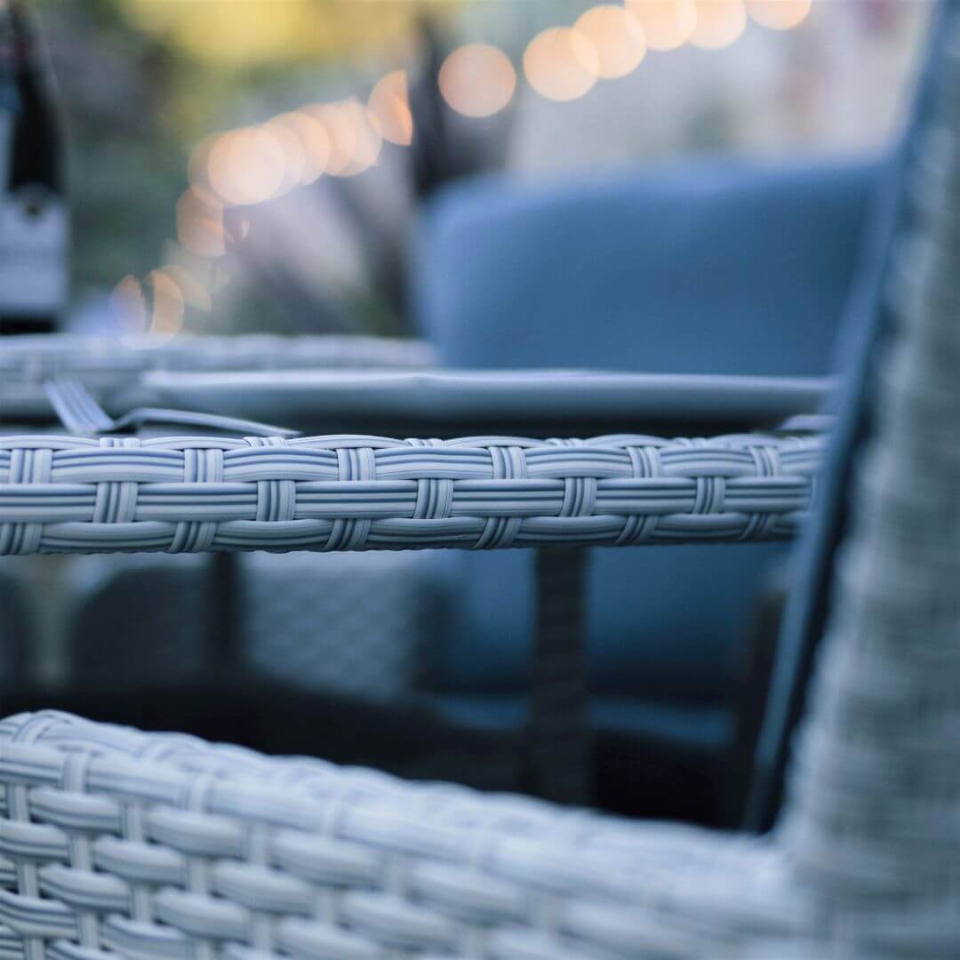 Close up of a light grey rattan round dining table and an arm of a dining chair.