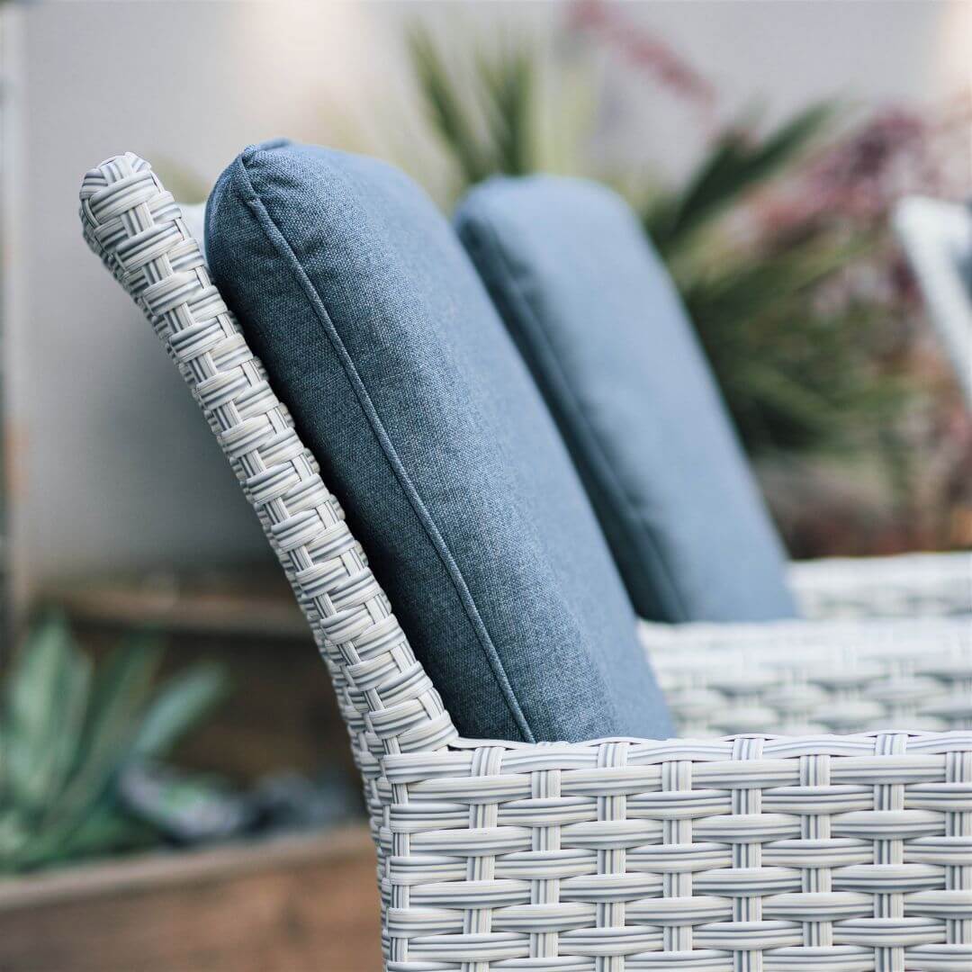 Close up of a light grey rattan dining chair with padded back cushion.