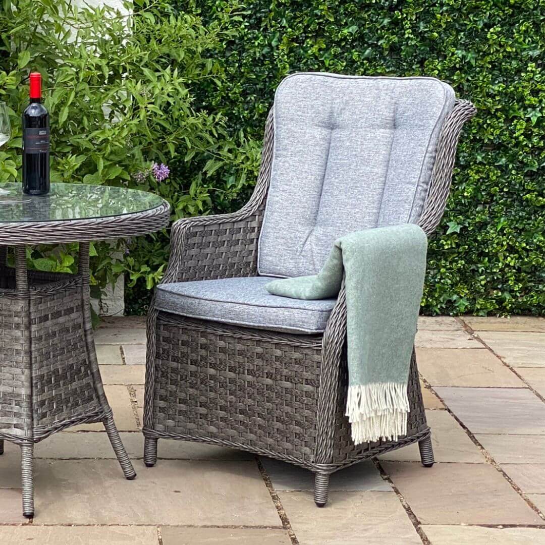 Close up of a dark grey rattan armchair with padded back and seat cushions and a small round table.